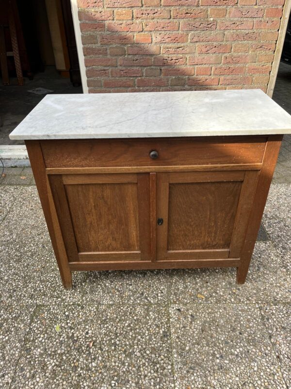 Kleine houten commode met wit marmeren blad – volledig naar wens af te werken Een prachtig kleinere commode met een echt wit marmeren blad — ideaal als commode in de babykamer, maar ook perfect voor in de hal of woonkamer als stijlvol opbergmeubel. Afmetingen: • Breedte marmeren blad: 95 cm • Diepte marmeren blad: 45 cm • Breedte commode: 87 cm • Werkhoogte wordt minimaal 90 cm — we plaatsen hiervoor eiken pootjes van in totaal 22,5 cm hoogte Deze commode krijgt dus nog mooie eiken pootjes (zoals al onze commodes), zodat hij qua hoogte perfect is voor gebruik. Het marmeren blad heeft een zachte, wit doorleefde uitstraling en vormt een prachtig contrast met de houten kast. De commode kan in originele houtkleur blijven of volledig in kleur naar wens worden afgewerkt — inclusief keuze in knopjes of handgrepen. Kleine houten commode met wit marmeren blad