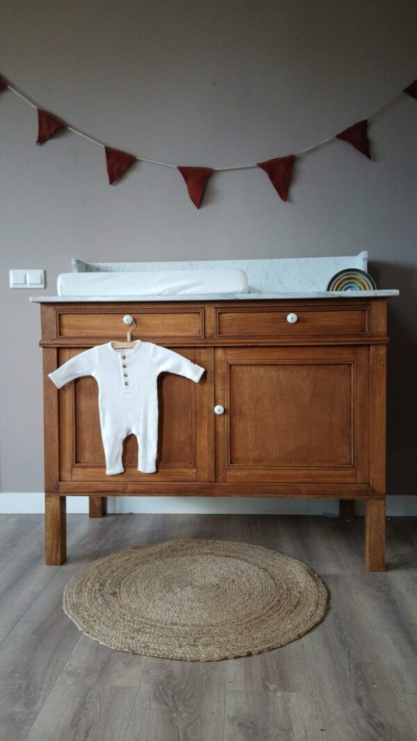 Breng warmte en karakter in de babykamer met deze prachtige vintage commode. Het meubel is uitgevoerd in massief hout met een rijke, warme tint en verfijnde details, waardoor het niet alleen praktisch is, maar ook een echte blikvanger. De commode biedt volop opbergruimte dankzij de ruime lades en het kastgedeelte, ideaal voor het netjes organiseren van kleertjes, verzorgingsproducten en accessoires. Het stevige blad is perfect geschikt als verschoonplek en combineert functionaliteit met stijl. De tijdloze uitstraling maakt dit meubel eenvoudig te combineren met zowel moderne als klassieke interieurs. Of je nu gaat voor een rustige, natuurlijke sfeer of een speelse babykamer, deze commode past zich moeiteloos aan. Een duurzaam en stijlvol meubel waar je jarenlang plezier van hebt – praktisch in gebruik en mooi om naar te kijken.